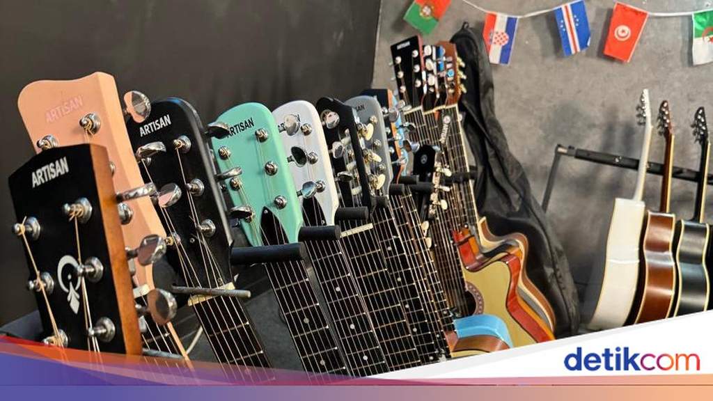 Seorang anak muda sedang serius belajar memainkan sebuah gitar akustik.